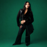 Beabadoobee, whose album 'Pylon' arrives in September, poses in an all-black outfit against a deep green backdrop.