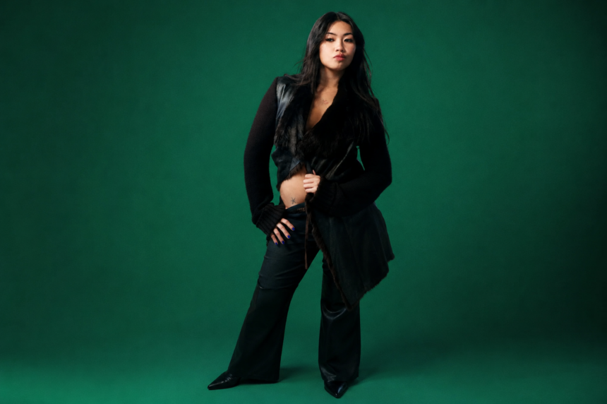 Beabadoobee, whose album 'Pylon' arrives in September, poses in an all-black outfit against a deep green backdrop.