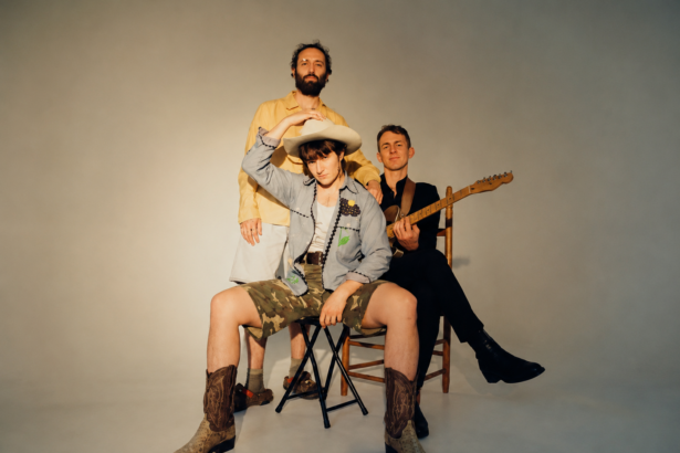 The members of Big Thief pose together in a studio, one seated in a cowboy hat and boots and another holding a guitar, in press art around their triple album 'Horsepower.'