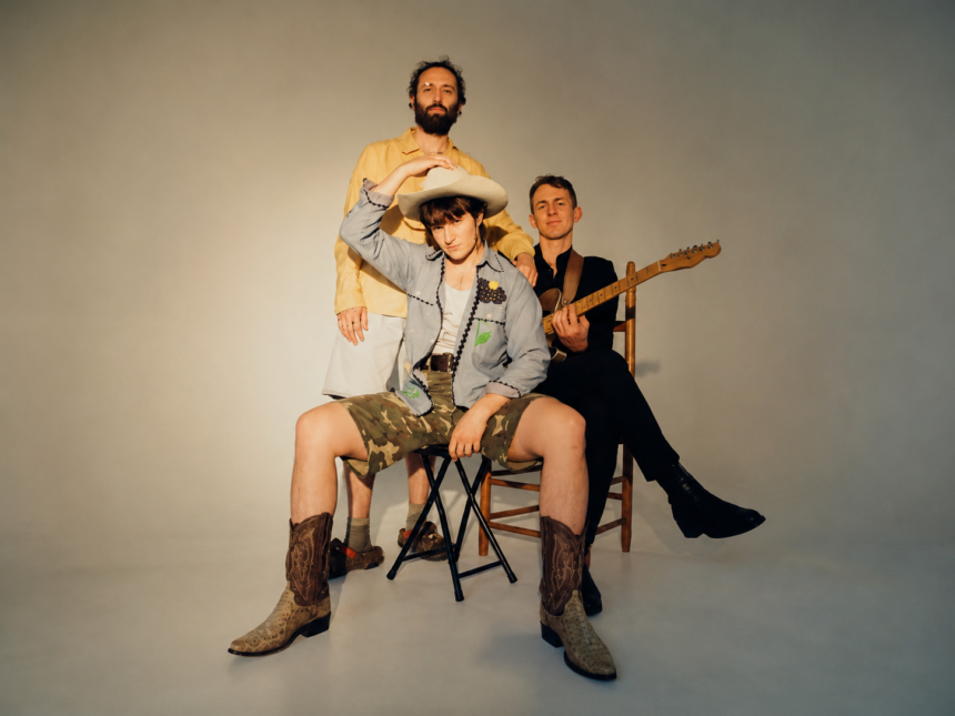 The members of Big Thief pose together in a studio, one seated in a cowboy hat and boots and another holding a guitar, in press art around their triple album 'Horsepower.'