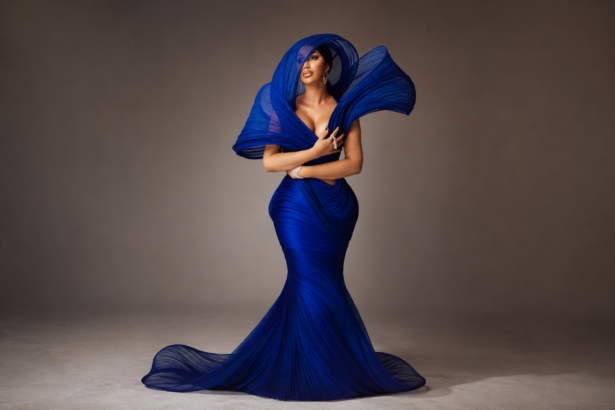 Cardi B poses in a dramatic pleated blue gown with a sculptural hood and diamond jewelry, in press art tied to her single 'Ah Ha.'