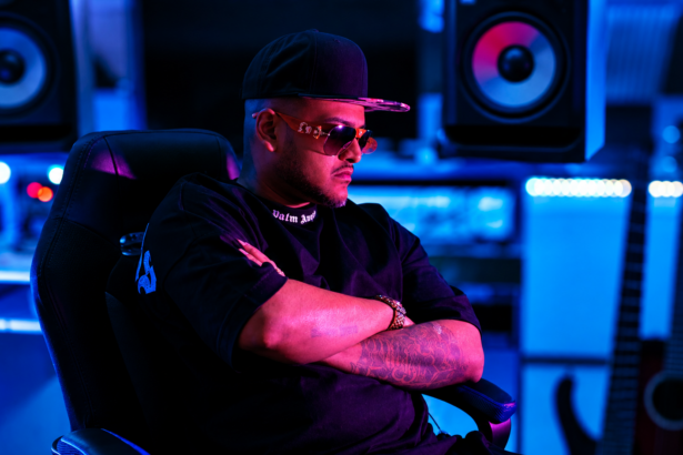 ChevoBeatz in a studio, arms crossed under blue and pink lighting.