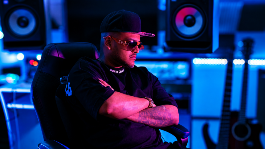 ChevoBeatz in a studio, arms crossed under blue and pink lighting.