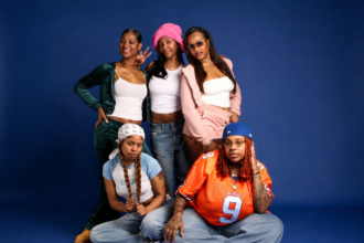 The five members of Cuzzos, the all-female South Central LA rap group, pose together against a blue backdrop in casual streetwear, in press art for their single 'Can't Pretend.'