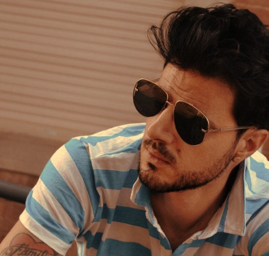 DJ Sparadise poses in aviator sunglasses and a blue-and-white striped polo shirt against a warm-toned backdrop, in press art for his single 'See U Again.'