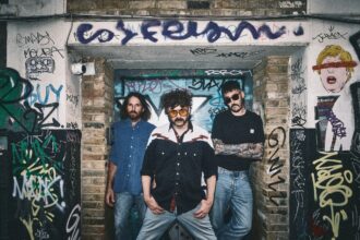 London trio Dead Horse pose in a graffiti-covered doorway, promoting their single 'I Would Die' from debut album 'Caught The Nonsense.'