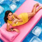 Dua Lipa reclines on a pink mat floating in a pool surrounded by giant ice cubes, sipping a drink in a yellow outfit, in a colorful press-style image.