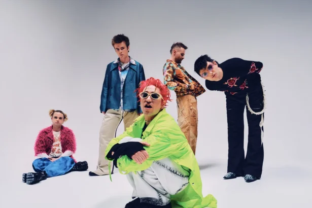 The five members of Fontaines D.C. pose in colorful, eclectic outfits against a plain grey backdrop, in press art for their 2026 arena tour and album 'Dopamine Chamber.'