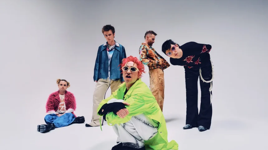 The five members of Fontaines D.C. pose in colorful, eclectic outfits against a plain grey backdrop, in press art for their 2026 arena tour and album 'Dopamine Chamber.'