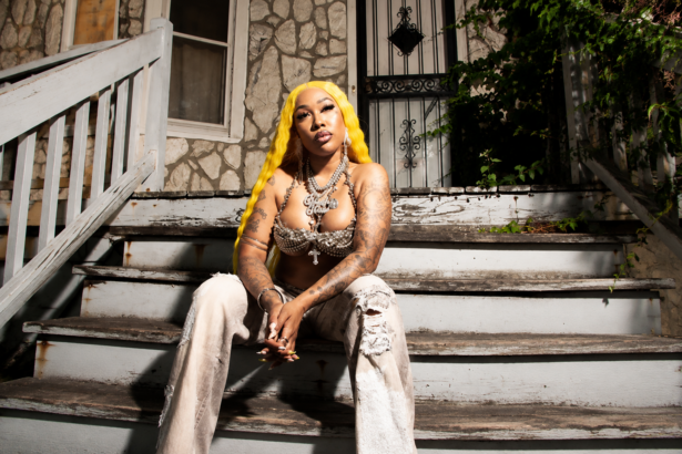 Glizzy Glow sits on a worn front stoop with bright yellow hair, tattoos, and layered jewelry, in press art for her debut mixtape 'Trench Baddie.'