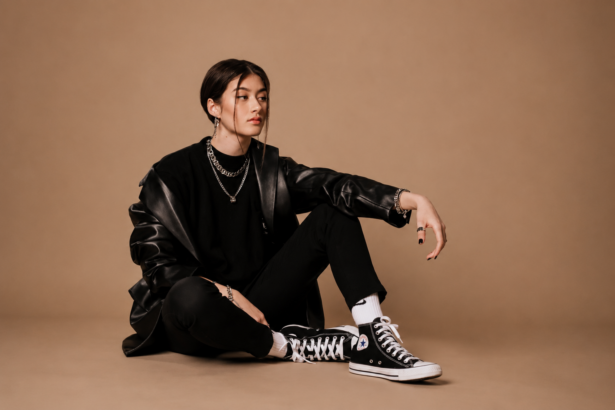 Press-style image for a Jade LeMac feature, showing a young woman in a black leather jacket and Converse high-tops seated against a tan backdrop.