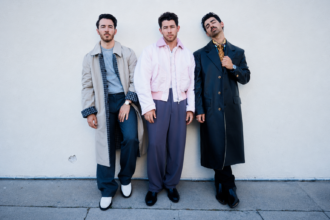 The Jonas Brothers, Kevin, Nick, and Joe, pose together in stylish coats and jackets, promoting their 'Burnin' Up All Over Again' 45-city anniversary tour.