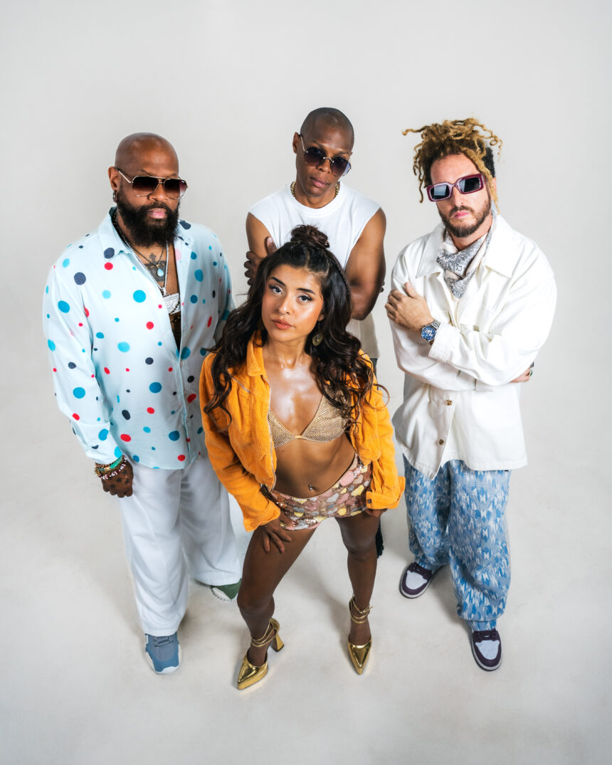 The four members of Latin collective Vale! ULB pose against a plain light backdrop in colorful, stylish outfits, with vocalist Val at the front, promoting their single 'Devórame.'