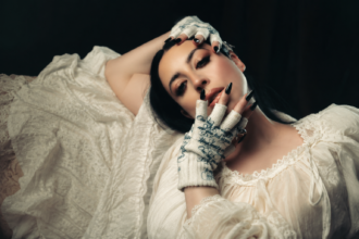 Madalen Duke, whose new single 'Sundown' with Caledo is out now, poses in a white lace dress and embroidered fingerless gloves.