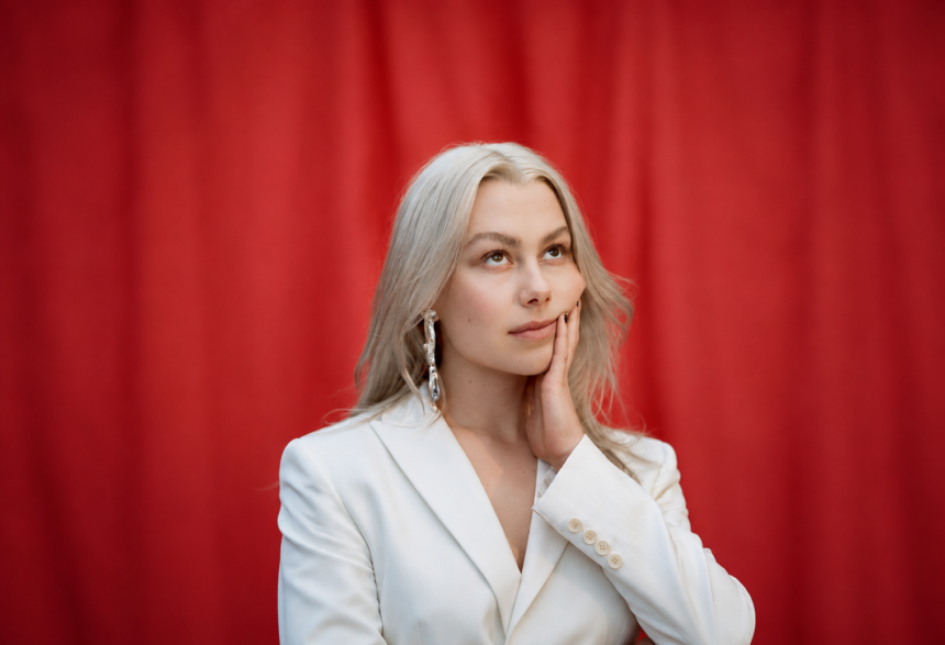 Phoebe Bridgers, whose album 'Lost Weekend' arrives Aug. 14, poses in a white blazer against a red curtain in a press portrait.