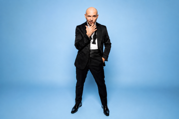 Pitbull poses in a sharp black tuxedo against a gray backdrop, promoting his 14th studio album 'Pitcoin.'
