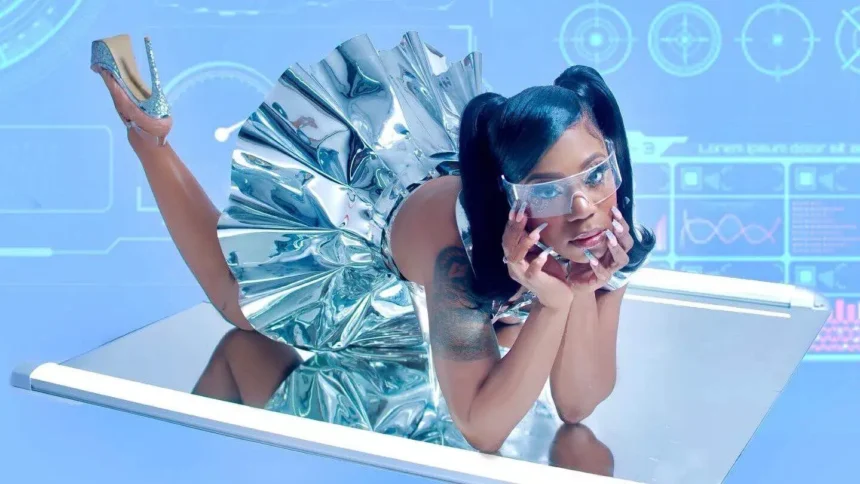 Rakiyah reclines on a mirrored surface in a metallic silver dress and futuristic visor, set against a blue sci-fi interface background, for her album 'My Collection of Boy Tears.'
