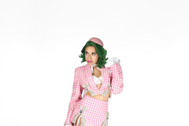 Slay Raché poses against a white backdrop with green hair and a pink beret, wearing a pink houndstooth cropped jacket and mini skirt with jeweled bows, promoting her single 'Sarasota.'