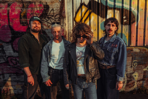 The four members of Bristol band Spin Class pose in denim and leather against a graffiti-covered wall at golden hour, in press art for their single 'Rip 'N' Dip.'