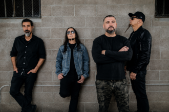 The four members of System of a Down lean against a grey cinderblock wall in dark clothing, promoting their one-night-only Maracanã Stadium concert in Rio de Janeiro.