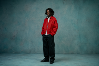 Nigerian Afropop artist Taves poses in a red jacket and black trousers against a teal backdrop, promoting his new EP 'Popstar SIDE A.'