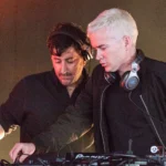 The Avalanches, who have announced their album 'No Bad Memories,' perform a DJ set behind Pioneer decks under warm stage lights.