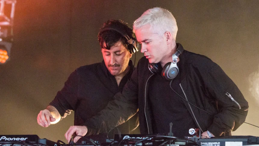 The Avalanches, who have announced their album 'No Bad Memories,' perform a DJ set behind Pioneer decks under warm stage lights.