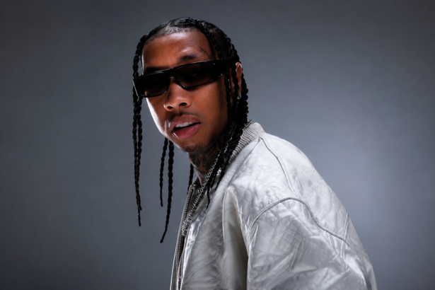 Tyga, who confirmed AI helped shape his album '$tarface,' poses in sunglasses and a silver jacket in a press portrait.