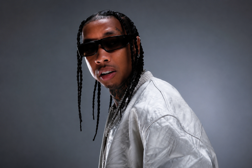 Tyga, who confirmed AI helped shape his album '$tarface,' poses in sunglasses and a silver jacket in a press portrait.