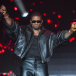 Usher, who shut down viral 'clone' rumors from his R&B Tour, performs onstage in a black leather jacket with arms outstretched.