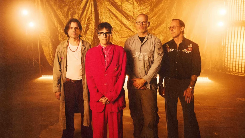 Weezer, whose single 'C.E.O.' precedes The Gold Album, pose against a gold backdrop with Rivers Cuomo in a red suit at center.