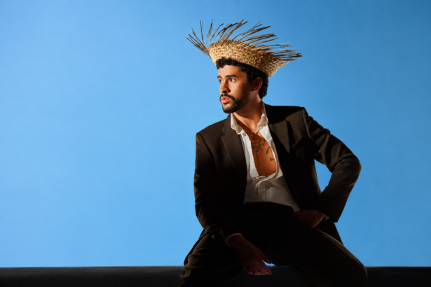 Bad Bunny sits in a black suit and woven straw hat against a blue backdrop, in press art tied to his first Emmy win for the Super Bowl LX Halftime Show.