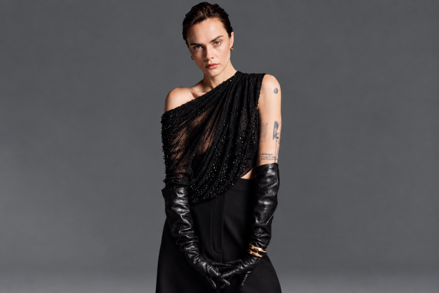 Cara Delevingne poses for Harper's Bazaar in a black off-shoulder beaded gown with long black leather gloves, her hair slicked back and arm tattoos visible.