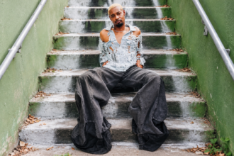 Rapper in distressed denim and baggy jeans on concrete steps, illustrating Danny Brown's 'Atrocity Exhibition' anniversary