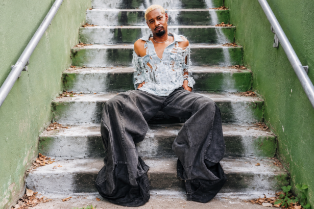 Rapper in distressed denim and baggy jeans on concrete steps, illustrating Danny Brown's 'Atrocity Exhibition' anniversary