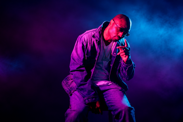 Chicago rapper Don Che posing in a denim jacket and chain under pink and blue studio lighting