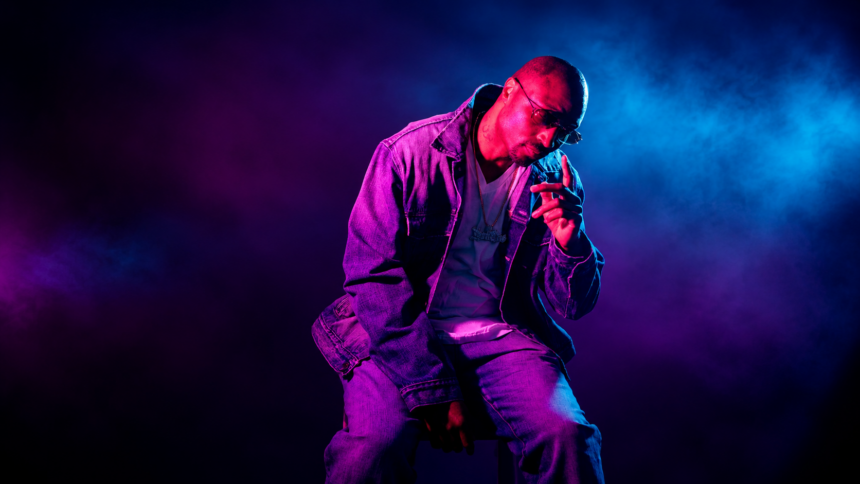 Chicago rapper Don Che posing in a denim jacket and chain under pink and blue studio lighting
