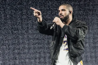 Drake performs onstage with a mic, pointing to the crowd in a denim jacket and Lakers jersey against an LED backdrop, tied to his surprise 'ICEMAN' set at Don Toliver's Toronto show.
