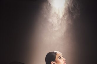 Mila Sidhu in profile wearing a black lehenga, maang tikka and chandbali earrings under a beam of light