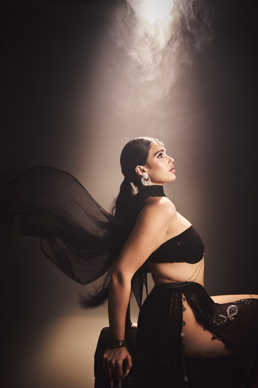 Mila Sidhu in profile wearing a black lehenga, maang tikka and chandbali earrings under a beam of light