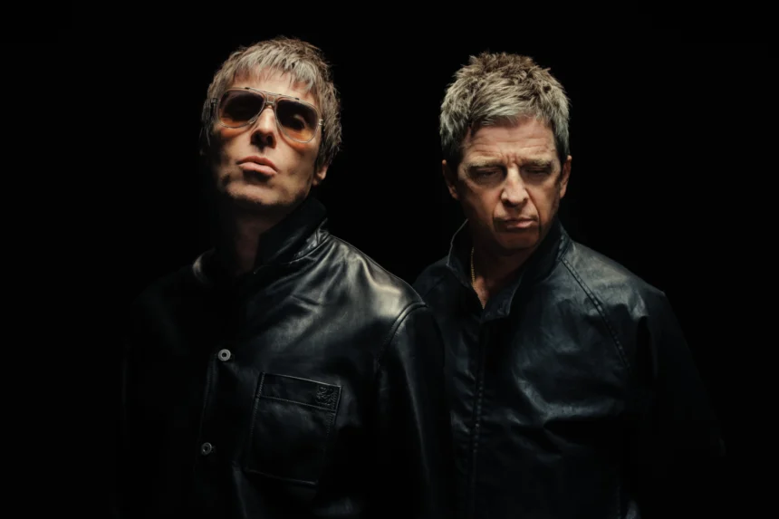 Liam and Noel Gallagher of Oasis pose against a black background in black leather jackets, Liam in tinted aviator sunglasses, both with signature moody expressions.