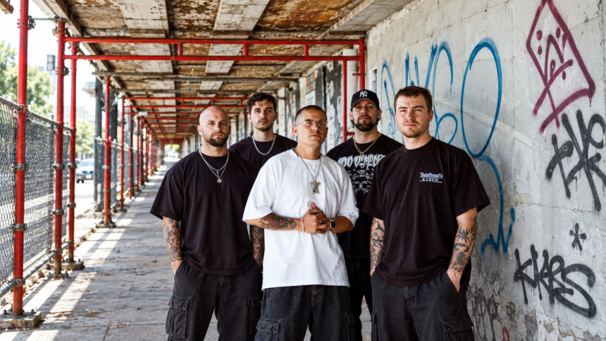 The five members of Pain Of Truth stand together in a graffiti-covered urban walkway with red scaffolding, wearing dark streetwear and chains, their expressions serious.