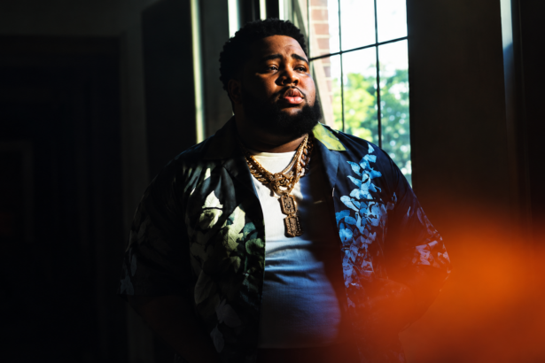 Rod Wave stands by a window in a patterned jacket and gold chains in dramatic low light, in press art tied to his No. 1 album 'Don't Look Down.'