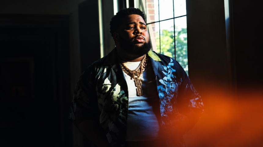 Rod Wave stands by a window in a patterned jacket and gold chains in dramatic low light, in press art tied to his No. 1 album 'Don't Look Down.'