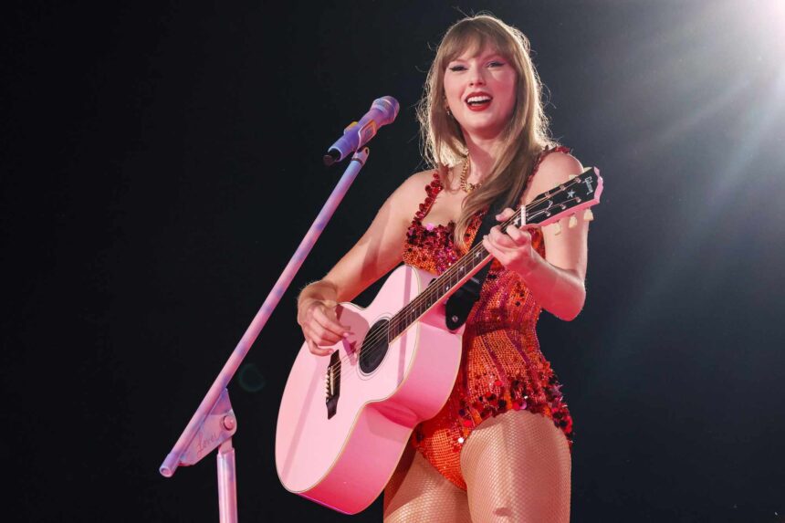 Taylor Swift performing on the Eras Tour in a red sequinned bodysuit, playing a pink acoustic guitar