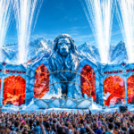 Tomorrowland Winter 2027 poster showing the festival's lion mainstage against snowy mountains with pyrotechnics and a packed crowd, captioned March 20 to 27, 2027, Alpe d'Huez, France.