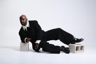 vincethealien reclines against cinder blocks in a black suit and ruffled white shirt on a white studio floor, in press art for the single 'Poisonous Child.'