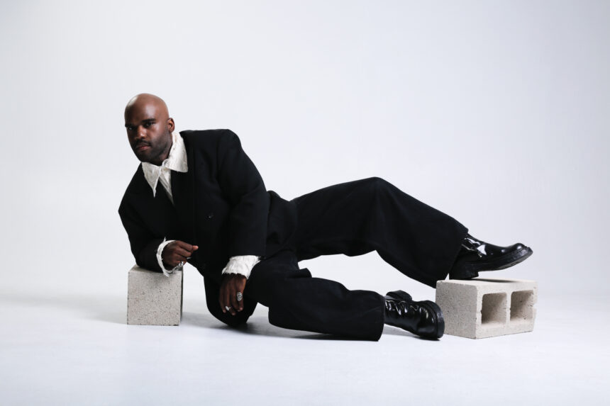 vincethealien reclines against cinder blocks in a black suit and ruffled white shirt on a white studio floor, in press art for the single 'Poisonous Child.'