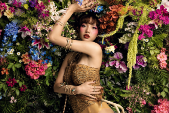 BLACKPINK’s LISA poses against a backdrop of vivid flowers in a gold scaled bodysuit, stacked gold-and-jewel bracelets and bold red makeup, in a promotional image for her ‘Press Play’ EP.