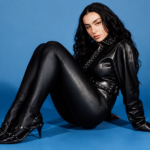 Charli XCX press photo in black leather against a blue backdrop, 'Music, Fashion, Film' Tour era.